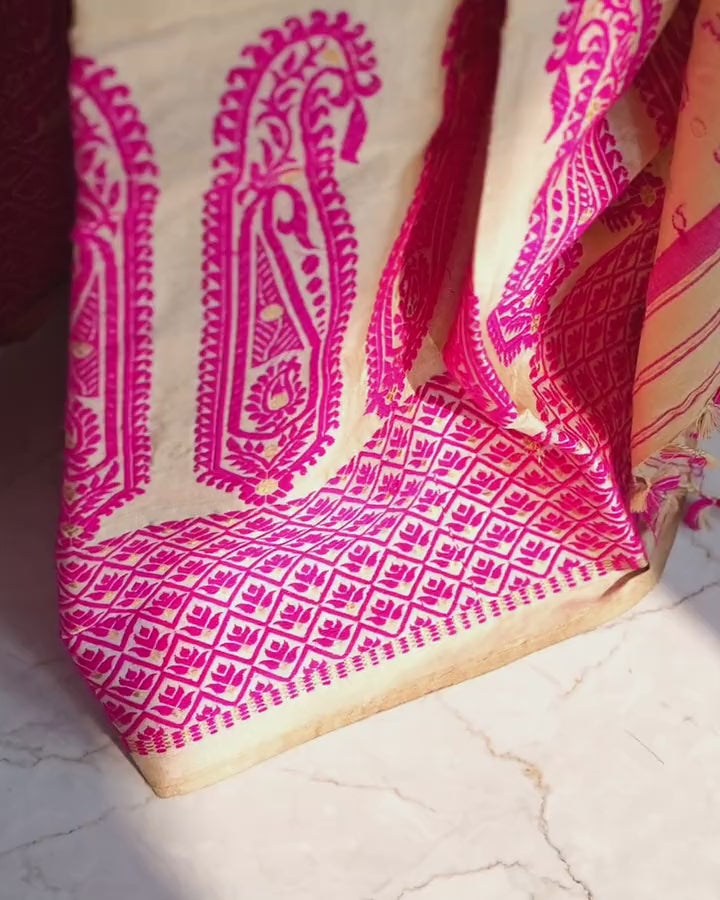 The mekhela hem on a sunlit marble floor: tall pink paisleys over the diamond border, the camera drifting slowly up.