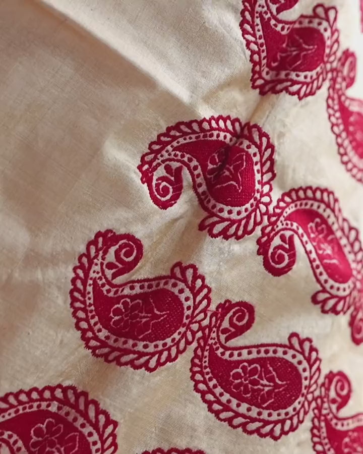 Rows of red paisleys on the mekhela, close, the cloth shifting slightly; each holds a cream flower inside a ring of dots.