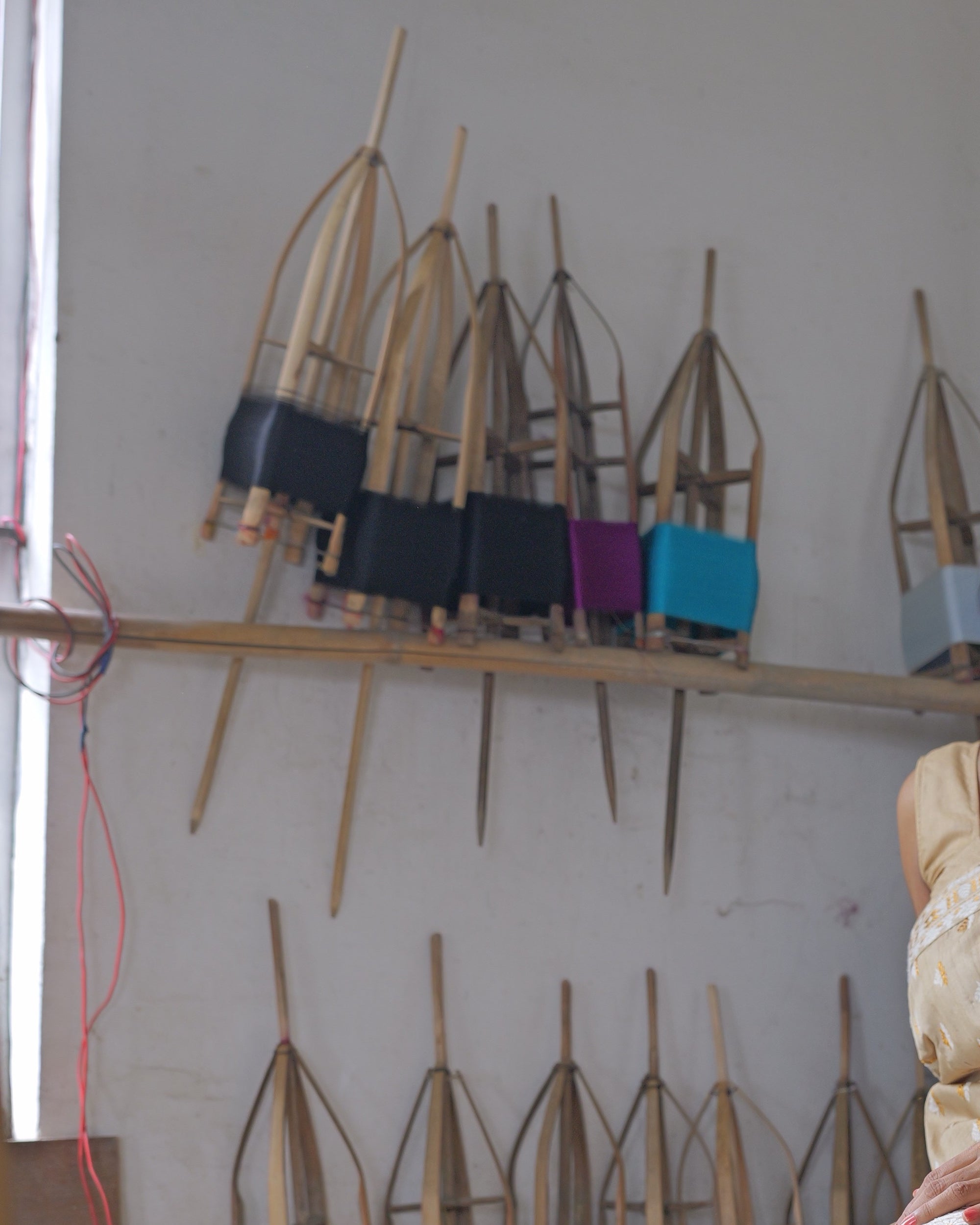 A wall of bamboo bobbin winders, each wound with a different colour of yarn, above a rack of shuttles and reeds.